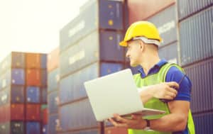 Worker man in hardhat and safety vest holding laptop and two-way radio, Foreman control loading containers box from cargo