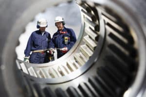 steel industry with two metal workers, engineers, seen through giant gear shafts