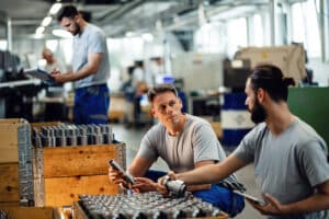  Two manual workers talking while cooperating during quality control inspection in steel factory.