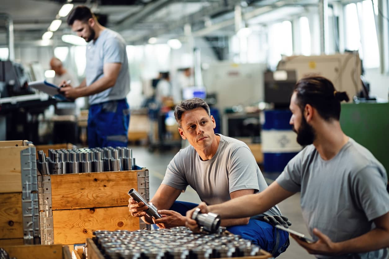 Two manual workers talking while cooperating during quality control inspection in steel factory.