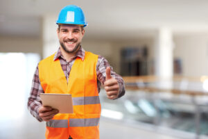 Smiling manual worker in blue helmet with digital tablet and gesture thumb up