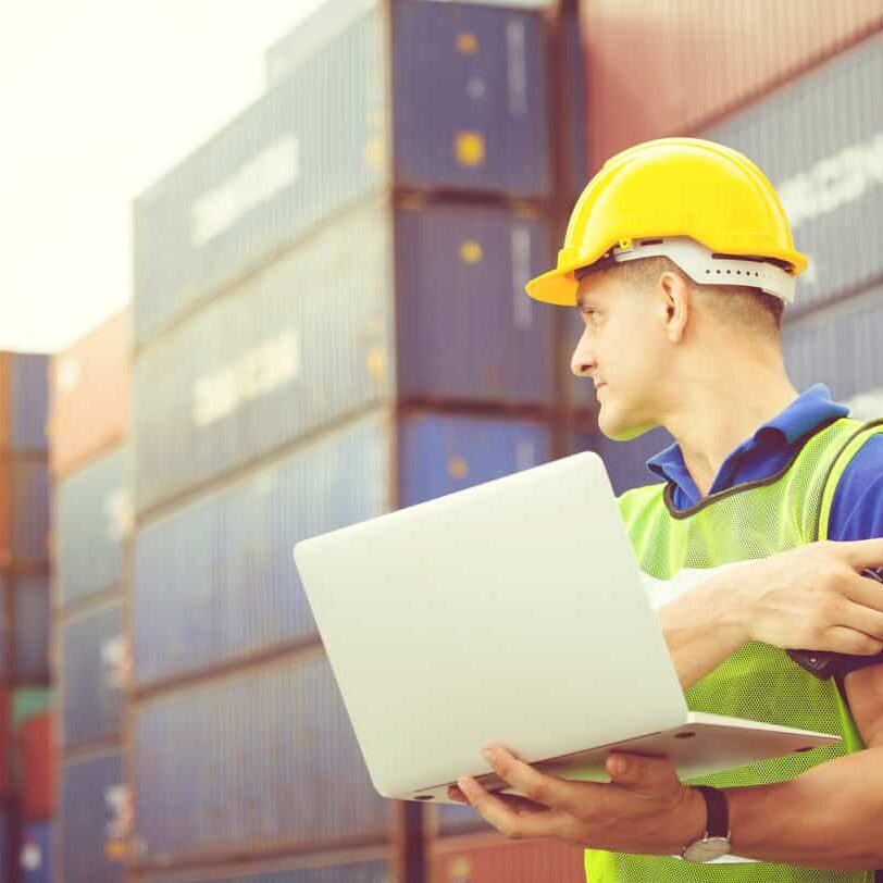 Worker man in hardhat and safety vest holding laptop and two-way radio, Foreman control loading containers box from cargo