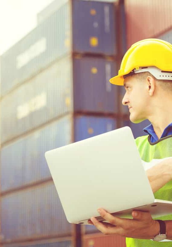 Worker man in hardhat and safety vest holding laptop and two-way radio, Foreman control loading containers box from cargo